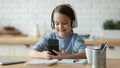 Smiling little girl wearing headphones using phone, distracted from studying Royalty Free Stock Photo