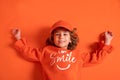 Smiling little girl 6-7 years old in cap and fashionable clothes lies on floor in the studio on orange background. Copy space