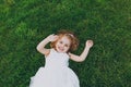 Smiling little pretty child baby girl in light dress lie on green grass lawn and spreading hands in park. Mother, little Royalty Free Stock Photo