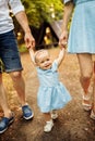 Smiling little toddler making first steps holding parents hands, cute baby girl in blue dress with mom and dad walk at Royalty Free Stock Photo