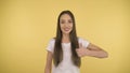 Smiling long-haired woman middle age having thumbs up on yellow background in studio. Middleweight woman in basic white