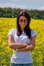 Smiling lovely brunette in sunglasses stay in rapeseed field. Royalty Free Stock Photo