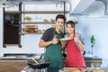 Smiling lovely young Asian couple with casual clothes is showing thumbs up and holding food plate after cooking together in modern Royalty Free Stock Photo