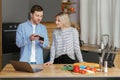 Smiling loving couple cooking salad together while standing on a kitchen at home and using mobile phone and laptop Royalty Free Stock Photo