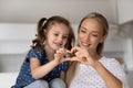 Smiling loving mother with adorable little daughter showing heart gesture