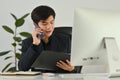 Smiling male accountant advisor holding open office binder and talking on mobile phone while sitting at workstation Royalty Free Stock Photo