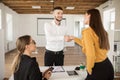 Smiling male applicant happily shaking employer hand. Young man in shirt getting new job after interview in modern