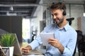 Smiling male business consultant with headphones sitting at modern office, video call looking at laptop screen