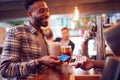 Smiling Male Customer In Bar Making Contactless Payment With Card For Drinks To Female Bartender