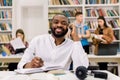 Smiling male dark skinned student working in a library. University student taking notes from book while sitting in the Royalty Free Stock Photo