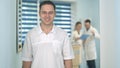 Smiling male doctor in glasses looking at camera while medical staff working on the background Royalty Free Stock Photo