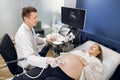 Smiling male doctor obstetrician, examining belly of happy pregnant woman by ultrasonic scan. Cheerful man doctor doing