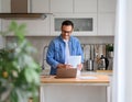 Smiling male financial adviser holding documents and working over laptop on kitchen counter at home Royalty Free Stock Photo