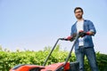 Smiling male gardener in protective glasses using lawn mower, while gardening in sunny day. Royalty Free Stock Photo
