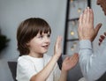 Smiling male kid rejoicing hitting palm clapping hands to woman nanny playing together