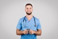 Smiling male nurse in blue scrubs holding a smartphone Royalty Free Stock Photo