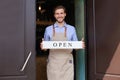 Smiling male owner of coffee shop is standing outdoors. He is holding placard and inviting everybody to come in. Open Royalty Free Stock Photo