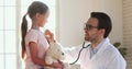 Smiling male paediatrician holding stethoscope examining cute little child girl