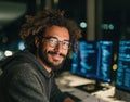Smiling male programmer with glasses coding software at night in a modern office setting Royalty Free Stock Photo