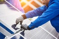 Smiling male technician in blue suit installing photovoltaic blue solar modules with screw.