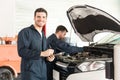 Technician Preparing Checklist While Colleague Inspecting Car In