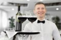 Smiling male waiter with glasses of red wine and a bottle on a tray in a restaurant Royalty Free Stock Photo