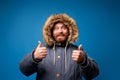 Smiling male in winter jacket with fur on empty blue background Royalty Free Stock Photo