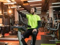 A smiling man with a beard rides a bike in the gym, listens to music and takes selfie