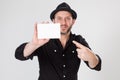 Smiling man in black shirt and black hat holding and pointing blank card