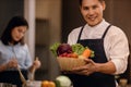 A Smiling Man with the Bowl of Fresh Vegetables, Preparing for Vegan Food in a Modern Kitchen. Blurred Woman Stirring a Healthy