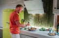 Smiling man cooking morning breakfast on the cozy home kitchen with a bright green fridge. He frying something delicious in the Royalty Free Stock Photo