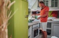 Smiling man cooking morning breakfast on the cozy home kitchen with a bright green fridge. He frying something delicious in the Royalty Free Stock Photo