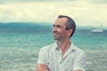 Smiling man with crossed arms by the sea, toothy smile middle ag