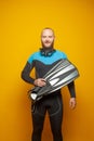 Smiling man diver standing holding fins on bright yellow studio background Royalty Free Stock Photo