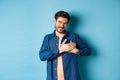 Smiling man feeling touched and grateful, holding hands on heart and thanking, standing on blue background