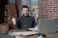 Smiling man freelancer raising hand in yes gesture, celebration victory, looking on laptop computer.