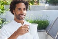 African American man wearing white polo shirt and sipping from ceramic mug on terrace with planters Royalty Free Stock Photo