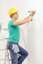 Smiling man in helmet hammering nail in wall Royalty Free Stock Photo