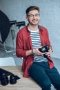 Smiling man holding camera and sitting on table with computer Royalty Free Stock Photo