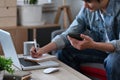 Smiling man holding mobile phone and making notes on notebook while working from home. Royalty Free Stock Photo