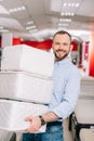 smiling man holding pile of folding mattresses in hands in furniture