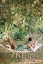Smiling man hugs the waist of woman lying on him in a hammock in a green garden