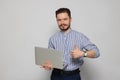 Smiling man with laptop showing thumbs up on grey background Royalty Free Stock Photo