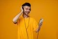 Smiling man listening music with headphones and mobile phone isolated over yellow wall Royalty Free Stock Photo