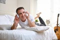 Smiling man listening music lying in bed window sunlight background