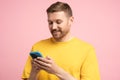 Smiling man looking at smartphone screen, browsing in internet chatting with friends over pink wall