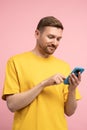 Smiling man looking at smartphone screen, browsing in internet chatting with friends over pink wall