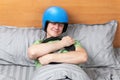 Smiling man in motorcycle helmet sleeping in bed clutching car steering wheel. Dreaming of racing.