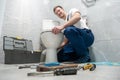 Smiling man plumber in uniform repairing toilet bowl using instrument kit looks happy professional repair service Royalty Free Stock Photo