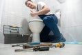 Smiling man plumber in uniform repairing toilet bowl using instrument kit looks happy showing like sign professional repair Royalty Free Stock Photo